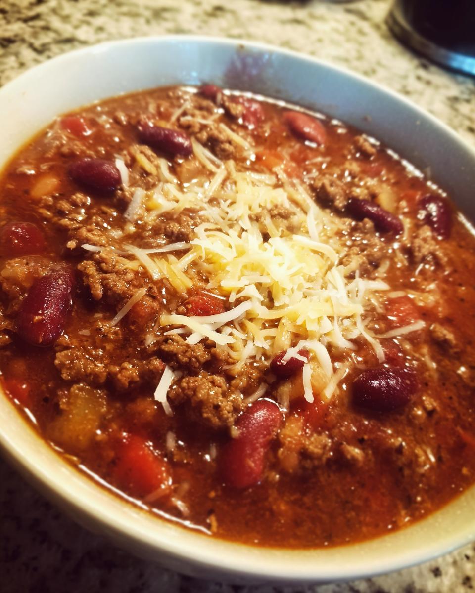 A close-up of a bowl of hearty slow cooker chili topped with shredded cheese.