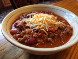 A close-up of a bowl of delicious slow cooker chili topped with shredded cheddar cheese.