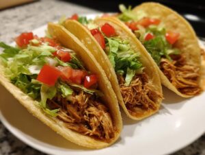 Three soft chicken tacos filled with shredded chicken, lettuce, and diced tomatoes.