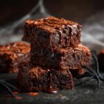 A stack of three fudgy spiderweb brownies drizzled with chocolate sauce, with a decorative spider.