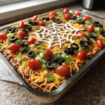 A festive Spiderweb Taco Dip topped with cherry tomatoes, black olives, and green onions.