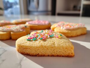 Close-up of heart-shaped sugar cookies decorated with white icing and colorful sprinkles.