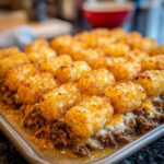 Close-up of a golden brown Tater Tot Casserole in a baking pan, with melted cheese and seasoned ground beef.