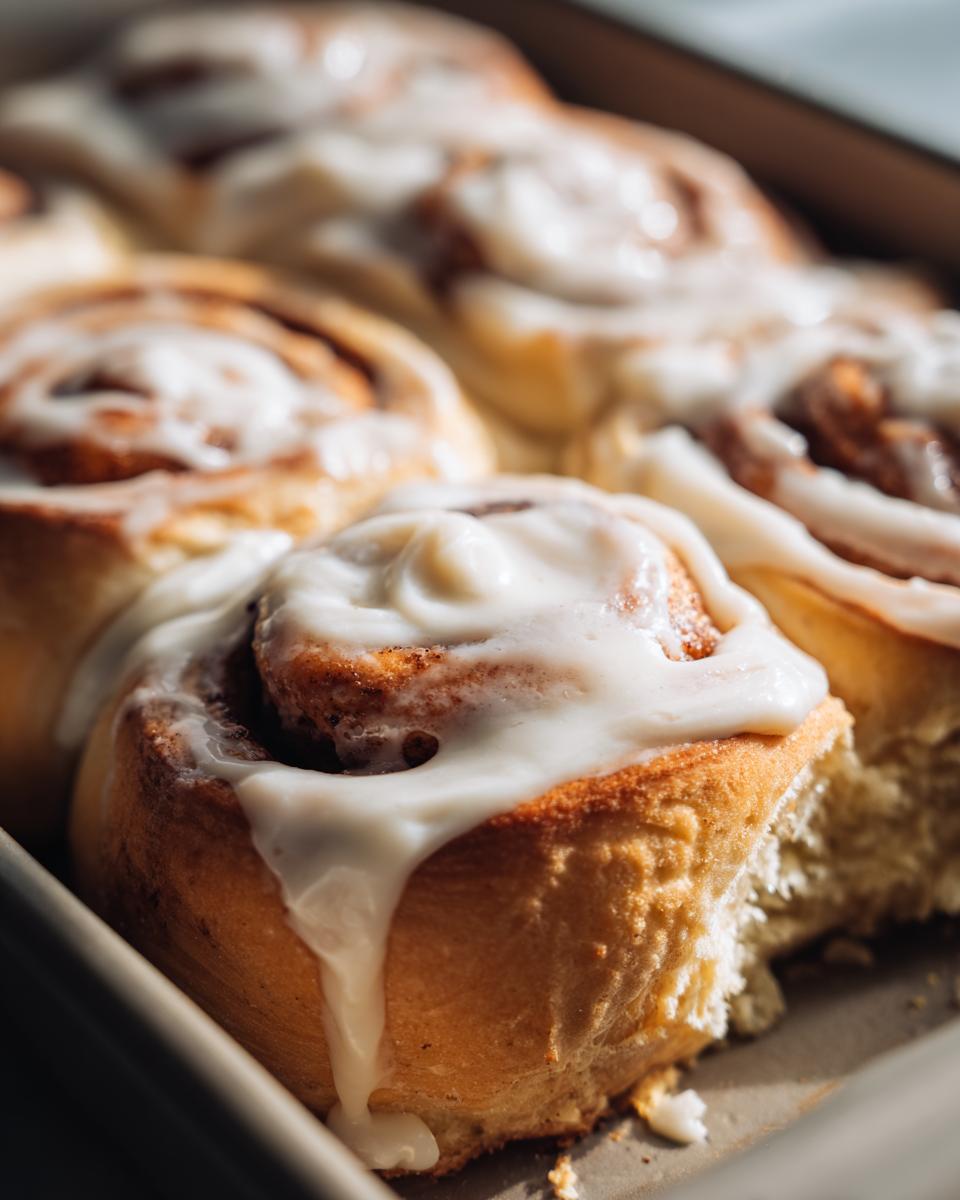 Close-up of fluffy cinnamon rolls drizzled with creamy white frosting in a baking pan.