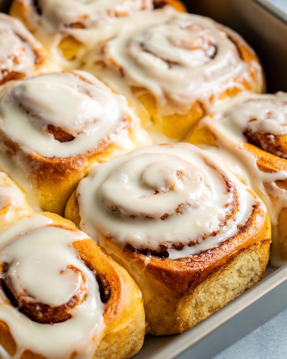 Close-up of freshly baked cinnamon rolls generously topped with creamy white frosting in a baking pan.