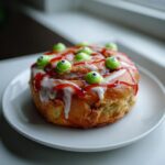 A single Zombie Cinnamon Roll decorated with white icing, red "blood" drizzle, and green candy eyes.