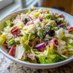 A close-up view of a hearty grinder salad featuring chopped lettuce, salami, cheese, red onion, and black olives.