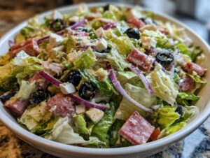 A close-up of a hearty grinder salad featuring lettuce, salami chunks, black olives, red onion, and white cheese cubes.