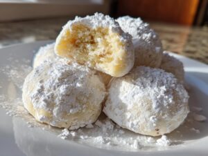 A close-up of several soft russian tea cakes heavily dusted with white powdered sugar on a white plate.