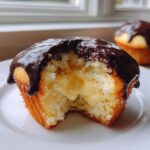 Close-up of a boston cream pie cupcakes cut in half showing vanilla cake, pastry cream filling, and chocolate ganache topping.