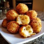 A pile of golden brown, crispy fried rice balls, with two broken open showing melted, gooey cheese inside.