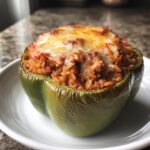 A single green stuffed bell peppers topped with melted cheese, served on a white plate.