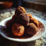 A pile of rich, cocoa-dusted chocolate truffles on a white plate, ready to be enjoyed.