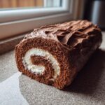 A close-up of a chocolate Yule log cake with a swirl of white cream filling, frosted with chocolate.