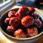 A close-up shot of a bowl filled with glistening cocktail meatballs in a rich, red sauce.