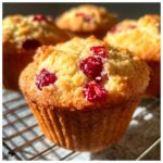 Close-up of golden-brown cranberry muffins studded with bright red cranberries, cooling on a wire rack.