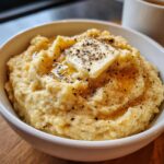 A close-up of creamy cauliflower mash topped with a pat of butter, melted butter, and cracked black pepper.