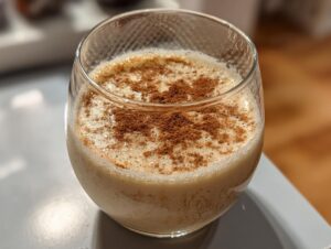 A close-up of a glass filled with creamy Coquito, topped with a generous dusting of cinnamon.