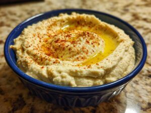 A close-up of creamy homemade hummus in a blue bowl, drizzled with olive oil and sprinkled with paprika.