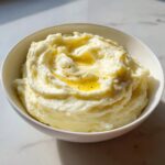 A bowl of fluffy mashed potatoes topped with melted butter and cracked black pepper.