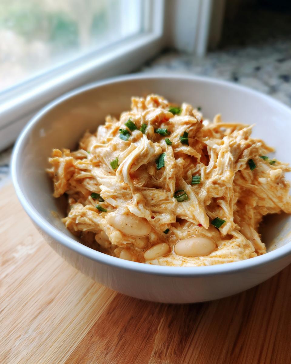 A close-up of creamy shredded chicken chili with white beans, garnished with chives, served in a white bowl.