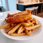 A golden, battered piece of fish resting on a generous serving of thick-cut chips, the classic fish and chips.