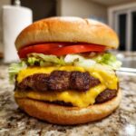 A tall, juicy double Cheeseburger featuring two seared patties, melted American cheese, shredded lettuce, and tomato on a soft bun.