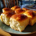 A plate of freshly baked, golden brown dinner rolls with a soft, fluffy interior.