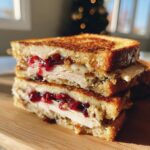Close-up of an epic turkey sandwich stacked high with sliced turkey, melted cheese, and cranberry sauce on toasted bread.