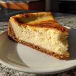 A perfect slice of creamy cheesecake with a golden-brown crust on a white plate.