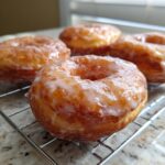 A close-up of several fluffy, golden-brown glazed donuts resting on a wire cooling rack.