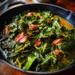 Close-up of hearty collard greens simmered with chunks of smoked meat in a cast-iron skillet.