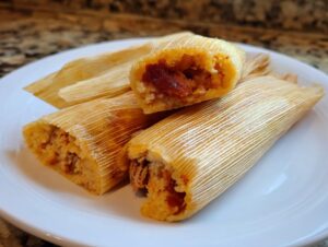 Close-up of three delicious homemade tamales on a white plate, one is cut open revealing the filling.