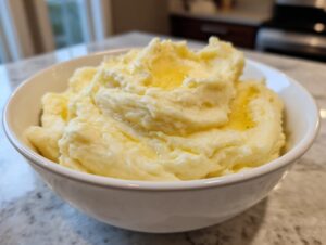 A close-up of a white bowl filled with fluffy mashed potatoes, topped with melted butter.