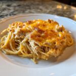 A close-up of a serving of creamy Monterey chicken spaghetti topped with bubbly, melted cheddar cheese.