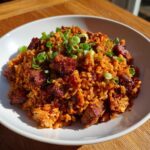 A close-up of rich, reddish-orange Jambalaya served in a white bowl, topped with chopped green onions.