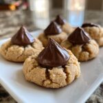 Close-up of delicious peanut butter blossoms cookies with chocolate kisses on top, arranged on a white plate.