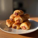 A delicious stack of golden-brown Pigs in a Blanket on a white plate, ready to be enjoyed.