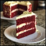 A slice of moist red velvet cake with layers of cream cheese frosting, showcasing its vibrant red color and rich texture.