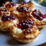 Close-up of several golden-brown cranberry brie bites with melted brie and dark red cranberry topping.