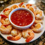 A plate of perfectly cooked shrimp cocktail arranged around a bowl of zesty red dipping sauce.