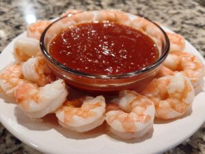 A plate of classic shrimp cocktail arranged around a bowl of red dipping sauce.