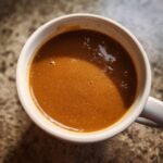 A close-up overhead view of a white mug filled with rich, smooth turkey gravy.