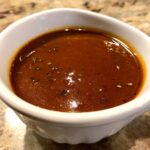 A close-up of a rich, dark vegetarian gravy in a white gravy boat, sprinkled with herbs.