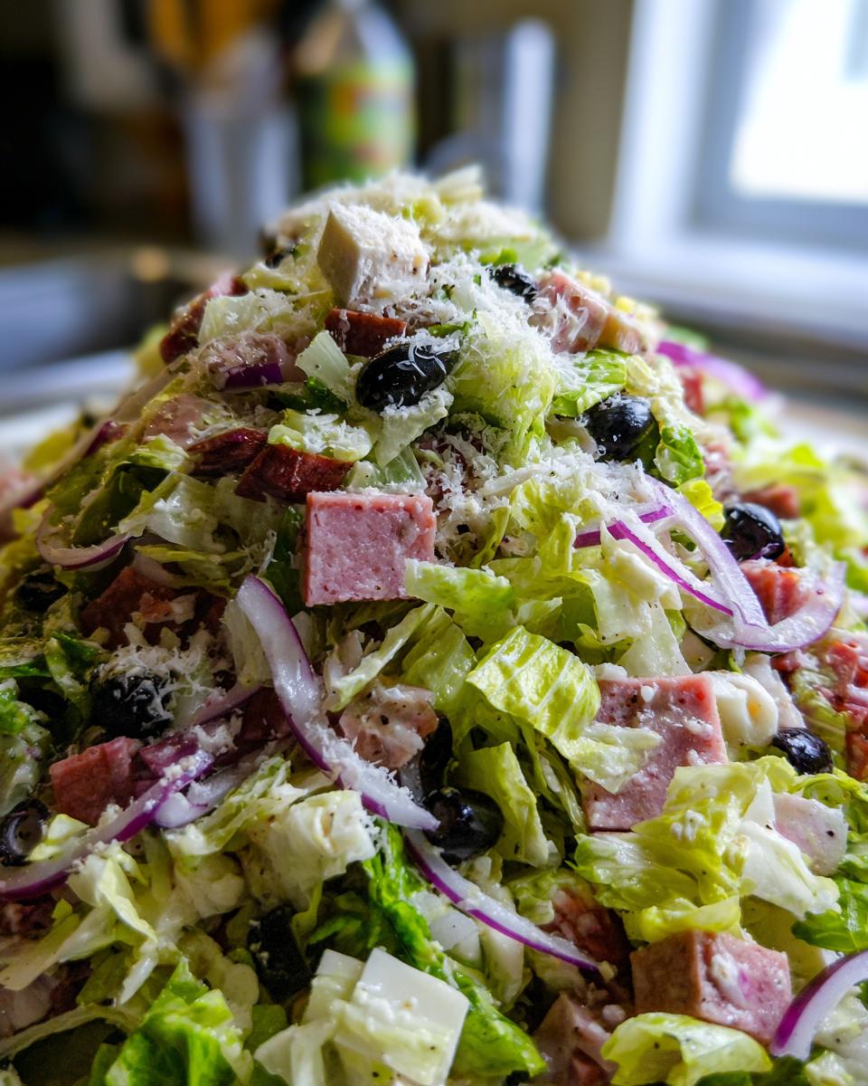 A close-up, towering mound of fresh grinder salad featuring chopped lettuce, cubed meats, black olives, red onion, and grated cheese.