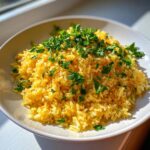 A close-up of bright yellow turmeric rice seasoned and generously topped with chopped fresh green parsley.
