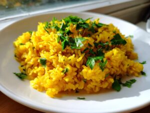 A serving of vibrant yellow turmeric rice topped generously with fresh, chopped green parsley on a white plate.
