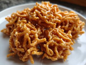 Close-up shot of several glossy, peanut butter-colored haystack cookies clustered on a white plate.