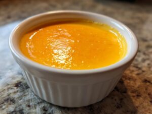 Close-up of smooth, bright orange beer cheese dip served warm in a small white fluted ramekin.