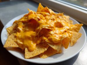 A close-up of tortilla chips smothered in bright orange nacho cheese sauce on a white plate.